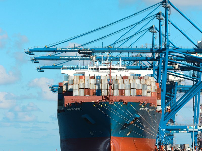 Container ship stacked with shipping containers moored beneath blue gantry cranes at a container terminal