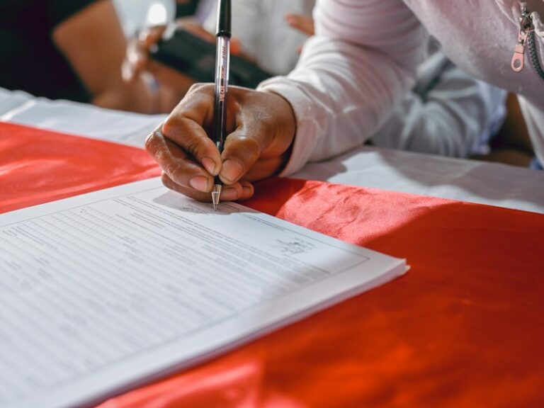 A person signing a printed form at a table with a pen